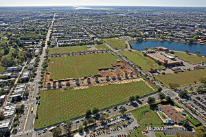 Luftbild einer Stadt mit Gebäuden, Bäumen, Gras, Straßen mit Fahrzeugen, Wasser und Wolken, das einen großen zentralen Bereich für einen Park vorsieht.