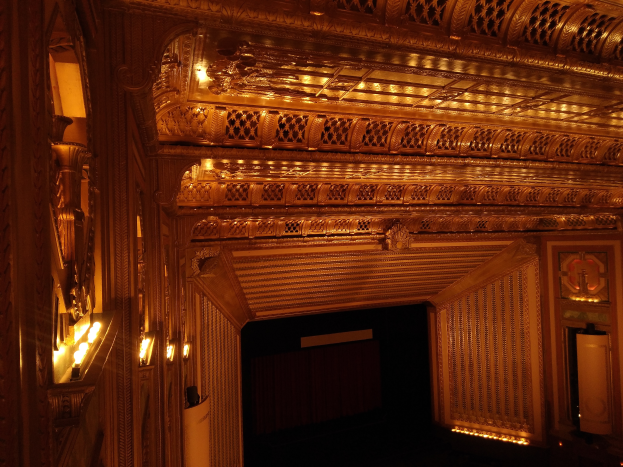 Ein prächtiger Theaterinnenraum mit dunklem Hintergrund, beleuchtet von beiden Seiten, mit einer kunstvoll gestalteten Decke.