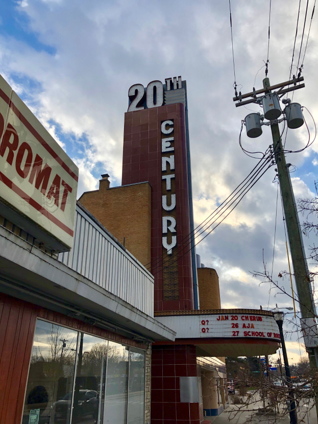 Au├čenansicht des 20. Jahrhundert Theaters in Detroit, Michigan, mit Glasw├Ąnden, Namensschildern, umgeben von B├Ąumen und Strommasten mit Dr├Ąhten unter einem bew├Âlktem Himmel.