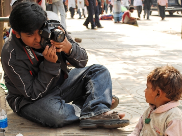 Ein Mann mit einer Kamera, mit Menschen auf der Straße und einer Flasche in der Szene.