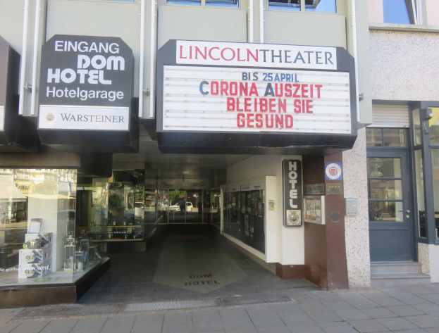 Außenansicht des Lincoln Theaters in Berlin, Deutschland, mit Glasfenstern und -türen sowie einer Schautafel und einem Blick ins Innere mit reger Aktivität.