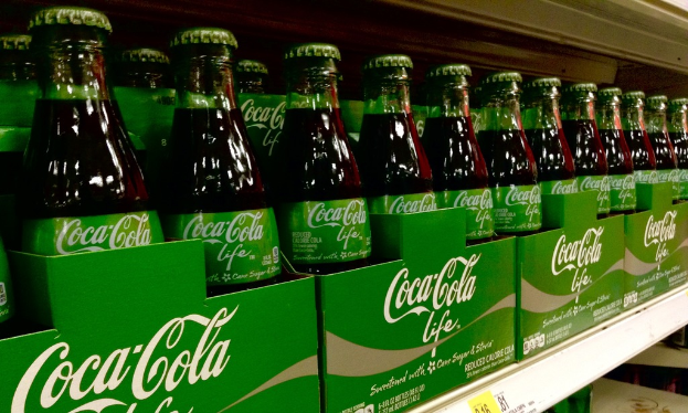 Glasflaschen werden in grünen Kartons mit 'Coca-Cola Life' daraufgestellt.