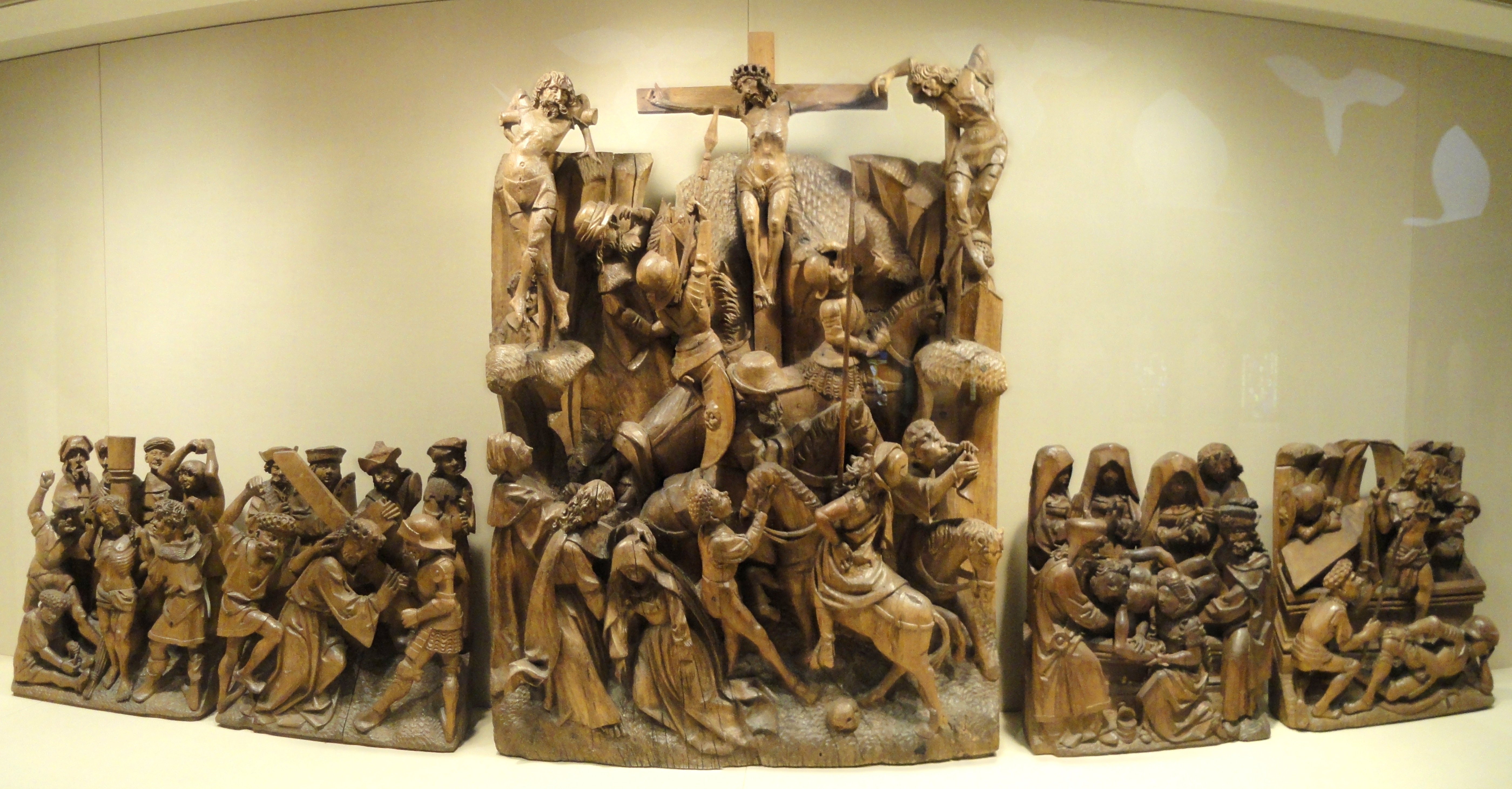 Eine Gruppe von Holzskulpturen, die gemeinsam in einem Museum ausgestellt sind, mit einer Wand im Hintergrund.