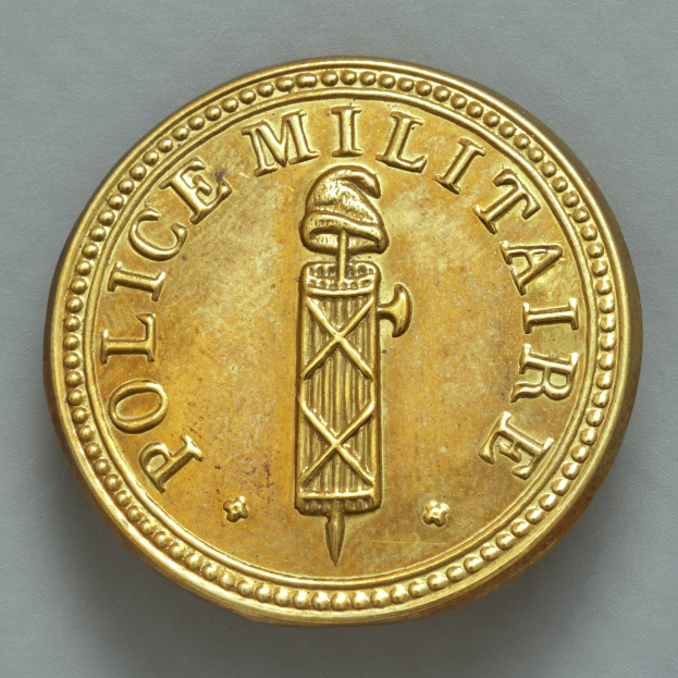 Eine Goldmünze mit der Aufschrift "Police Militaire" vor einem weißen Hintergrund.