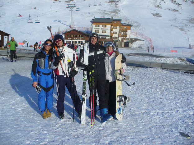Vier Personen posieren für ein Foto mit Schlittschuhausrüstung und Werkzeugen vor einer winterlichen Berglandschaft.
