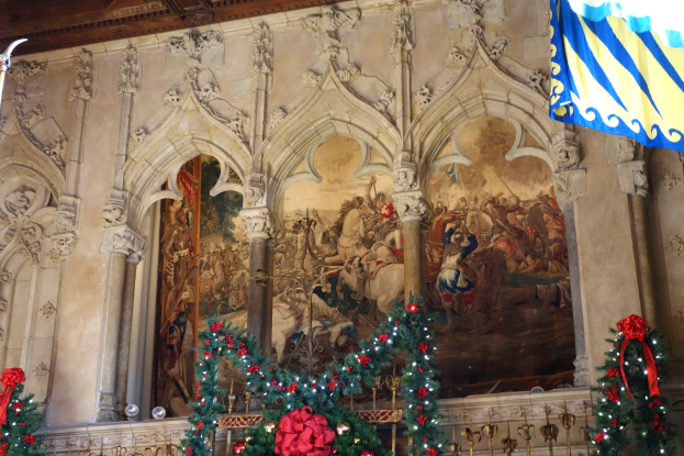 Kircheninneres mit einem Gemälde an der Wand, einer Flagge auf der rechten Seite, einem Geländer unten und einem geschmückten Weihnachtsbaum in der Mitte.