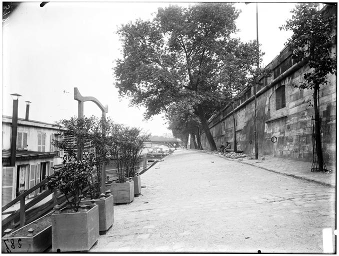 Eine Schwarz-Weiß-Aufnahme der New York State Penitentiary mit einer Wand auf der rechten Seite, Bäumen und Pflanzen auf der linken Seite und einer Brücke im Hintergrund, mit Text unten, der den Standort als New York City, New York, New Jersey, NY, USA identifiziert.