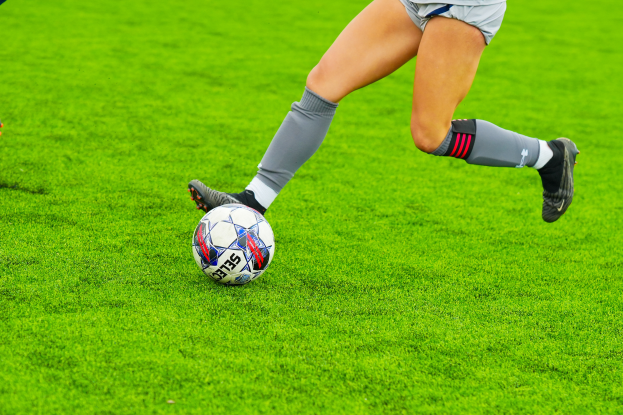 Eine Frau in einem Sportoutfit tritt einen Fußball auf einem saftigen grünen Feld.