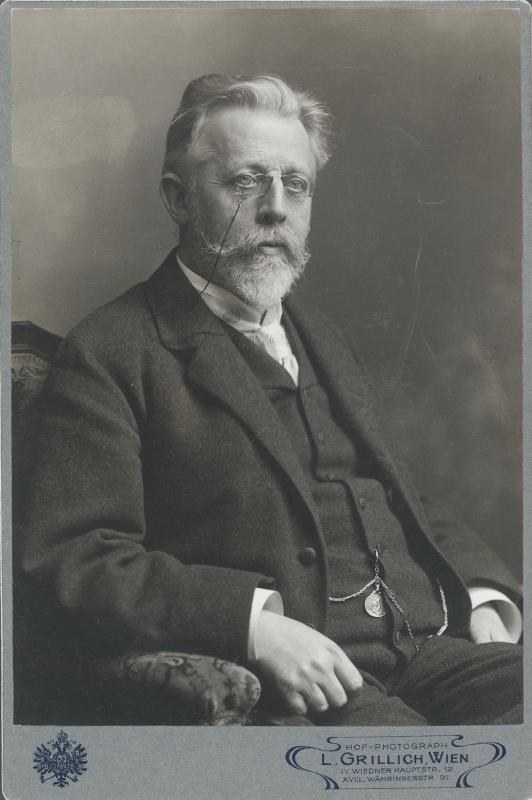 Schwarz-weiß-Fotografie eines bärtigen Mannes mit Brille, der auf einem Stuhl sitzt, mit Text unten, der ihn als "L. Grillich Wien, den Gründer der deutschen Revolution" identifiziert