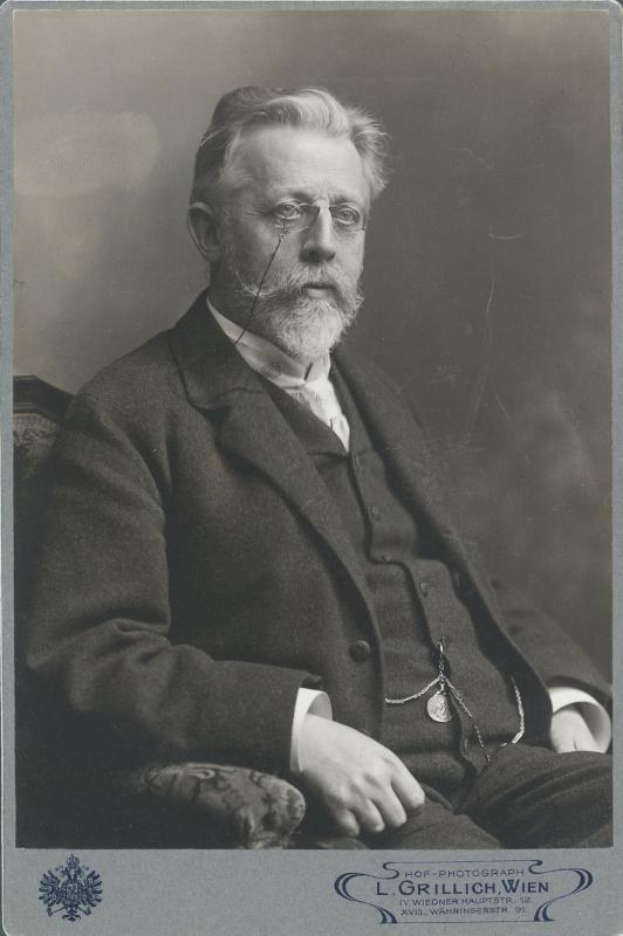 Schwarz-weiß-Fotografie eines bärtigen Mannes mit Brille, der auf einem Stuhl sitzt, mit Text unten, der ihn als "L. Grillich Wien, den Gründer der deutschen Revolution" identifiziert