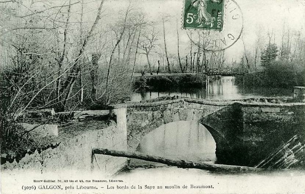 Ein altes Schwarz-Weiß-Foto einer baufälligen Brücke über einem Fluss, mit Bäumen auf beiden Seiten, einem Stempel oben drauf und Text unten.
