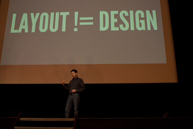 Eine Person steht auf einer Bühne und spricht, hinter ihr ist ein Bildschirm mit Text zu sehen.