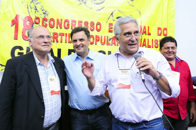 Ein Mann spricht in ein Mikrofon vor einem gelben Vorhang mit der Aufschrift "18-Grad-Kongress o", mit anderen Männern im Hintergrund.