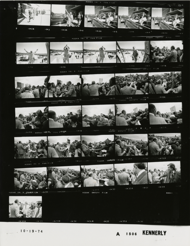 Ein Schwarz-Weiß-Foto einer vielseitigen Menschenmenge, die um einen Fernseher versammelt ist und strahlt.