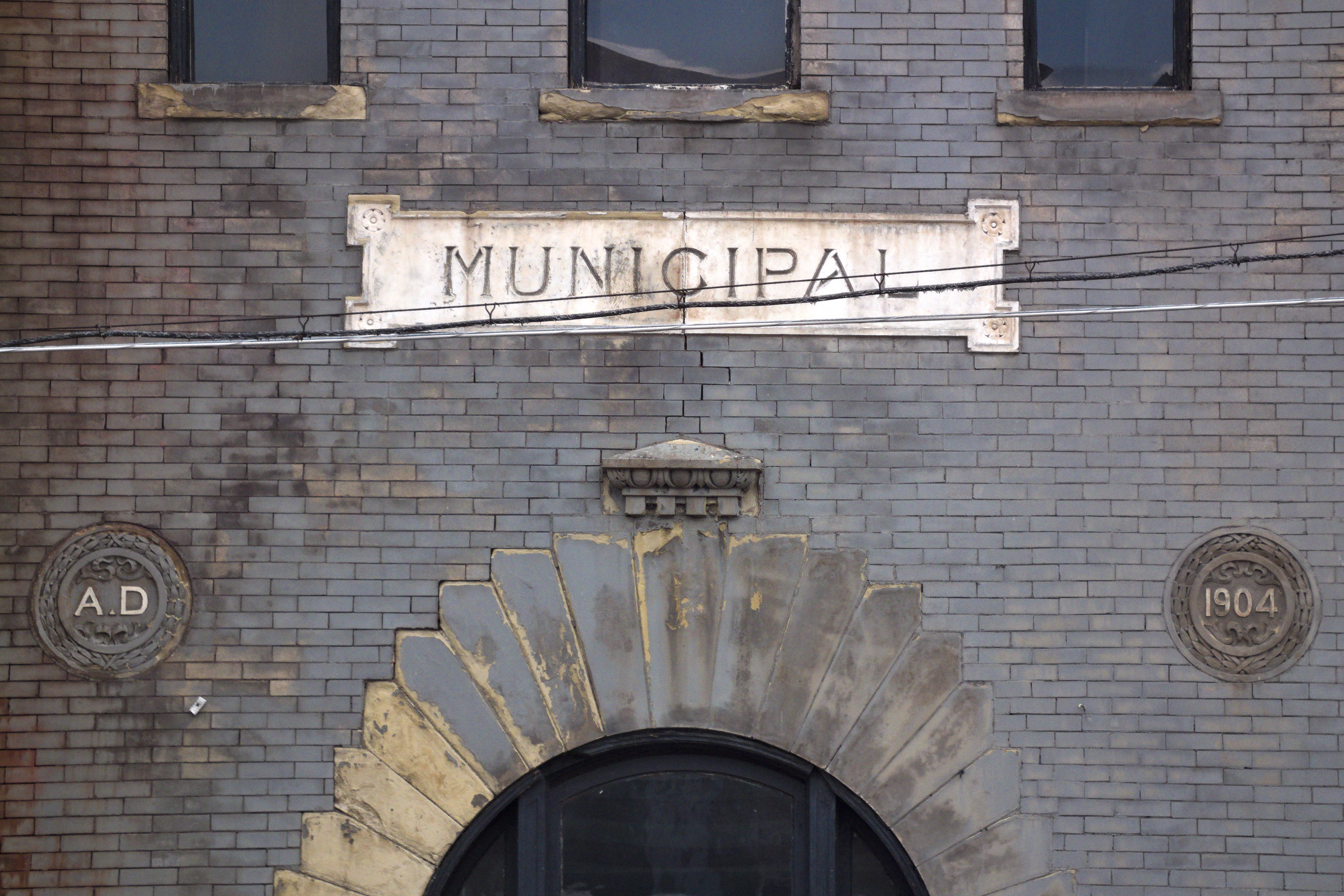 Ein Ziegelgebäude mit einer Seite, auf der ein Schild mit der Aufschrift 'Gemeinde' steht, mit einer Tür unten und Fenstern mit einem Namensschild oben.