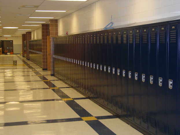 Eine lange Reihe von Spinden in einem Schulflur mit einem gefliesten Boden, einer Wand im Hintergrund, einer Decke mit Lampen oben und ein paar Gegenständen herumliegend.
