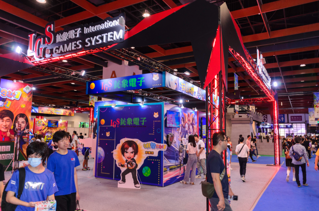 Eine Gruppe von Menschen geht durch einen Ausstellungssaal mit Ständen, trägt Taschen und hält Gegenstände, unter Deckenlampen mit einem Teppichboden, was eine Gaming-Messe in China suggeriert.