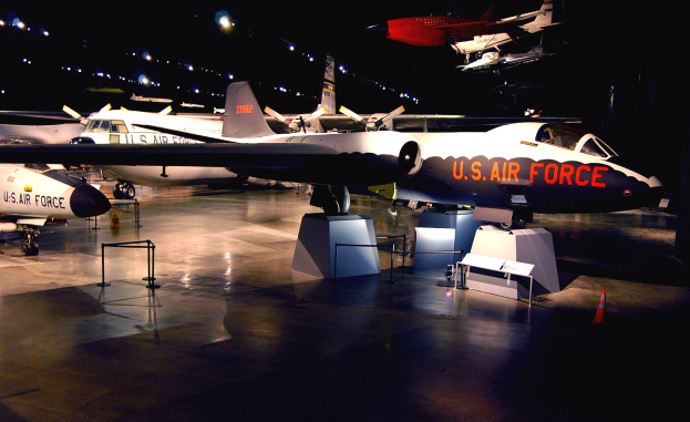 Eine Gruppe von Kampfflugzeugen in einem schwach beleuchteten Museum mit St├Ąnden, Verkehrskegeln und anderen Gegenst├Ąnden auf dem Boden.