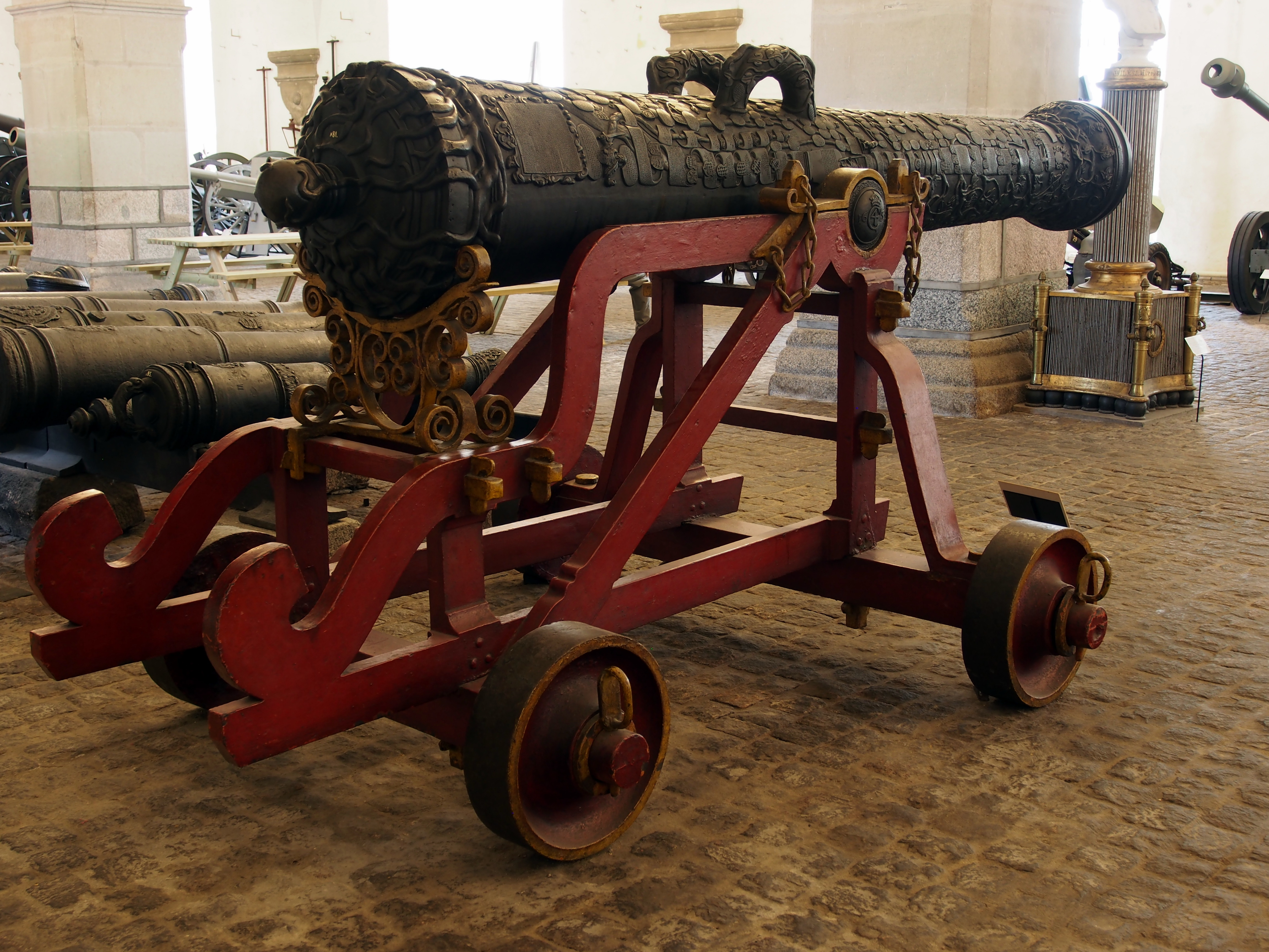 Eine alte Kanone in einem Museum ausgestellt, umgeben von anderen Kanonen und Pfeilern.