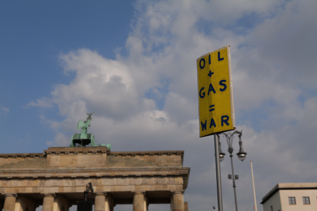 Das Brandenburgertor in Berlin, Deutschland, mit einem gelben Schild, das "Öl- und Gaskrieg" lautet, Gebäuden, Polen, Lampen, einer Statue und einem bewölkten Himmel im Hintergrund.