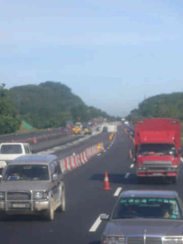 Eine Straße mit Verkehrskegeln, Leitplanken und Fahrzeugen, umgeben von Bäumen und Hügeln.
