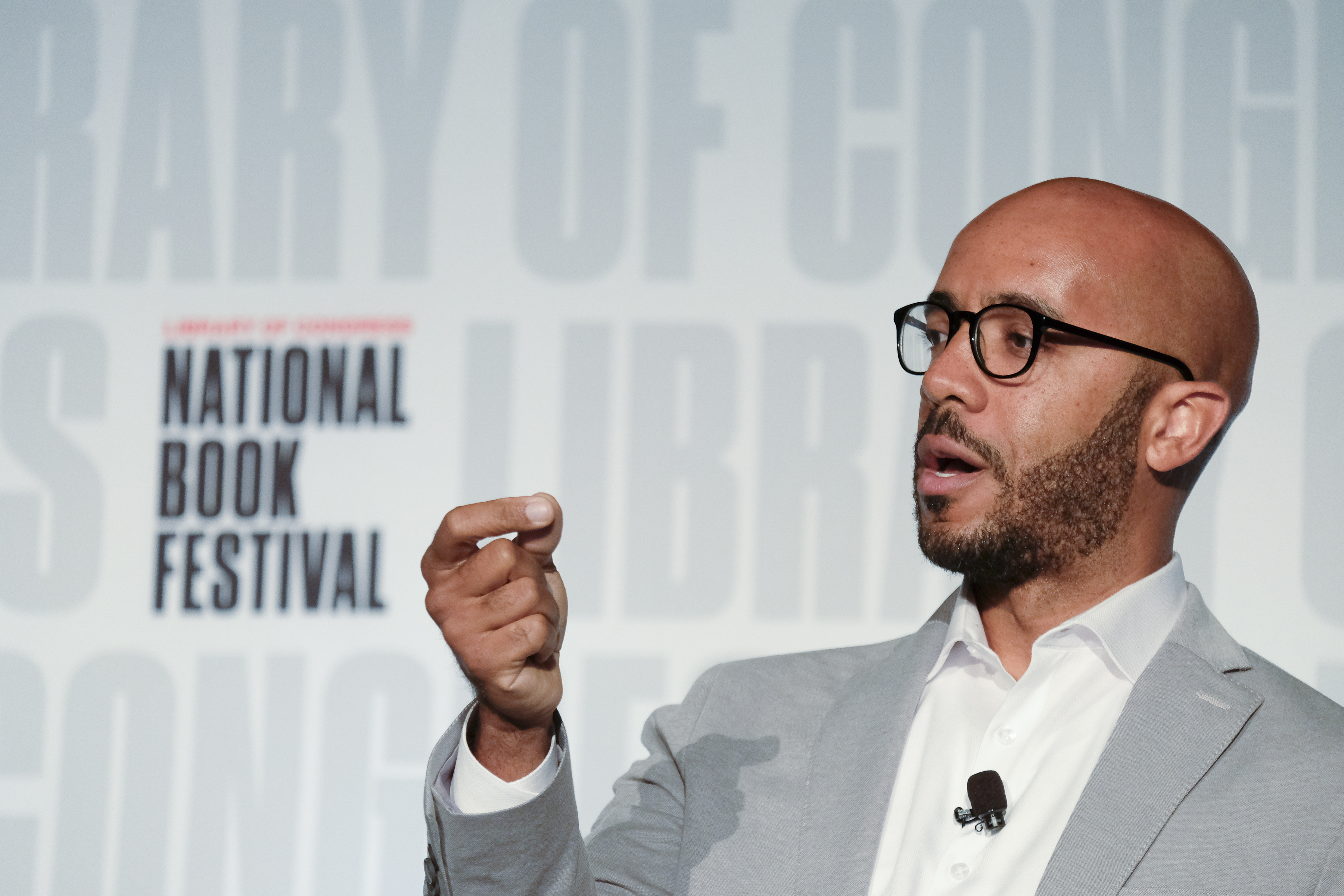 Ein Mann im Anzug und mit Brille spricht auf der Nationalen Buchmesse, trägt ein Mikrofon auf seinem Hemd.