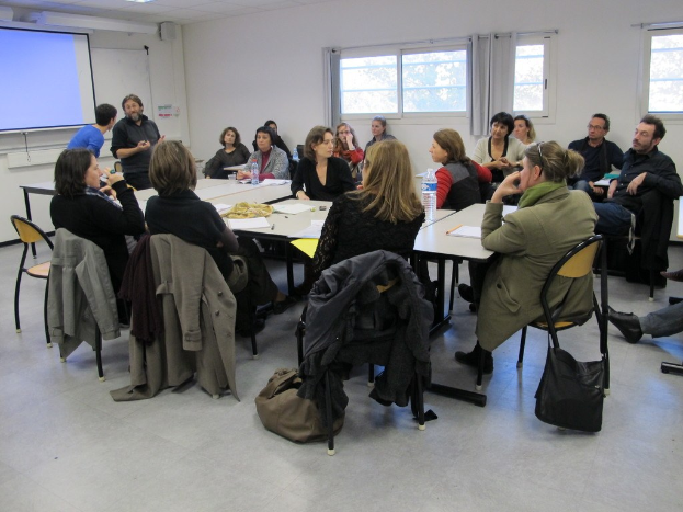 Gruppe sitzender Personen, die mit zwei stehenden Individuen diskutieren, die in der Nähe miteinander sprechen.