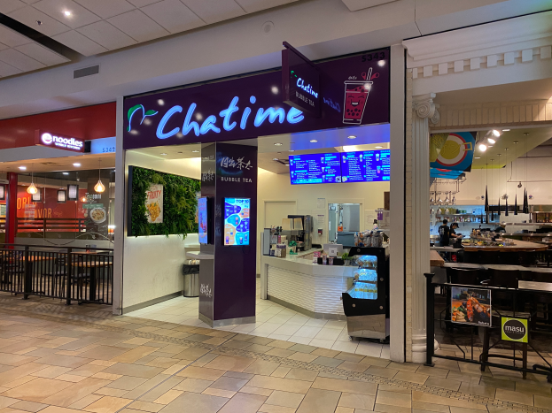 Ein Chatime-Restaurant in einem Einkaufszentrum mit Tischen, Stühlen, Geländern, Texttafeln, Bildschirmen, Lampen und sichtbarem Boden.
