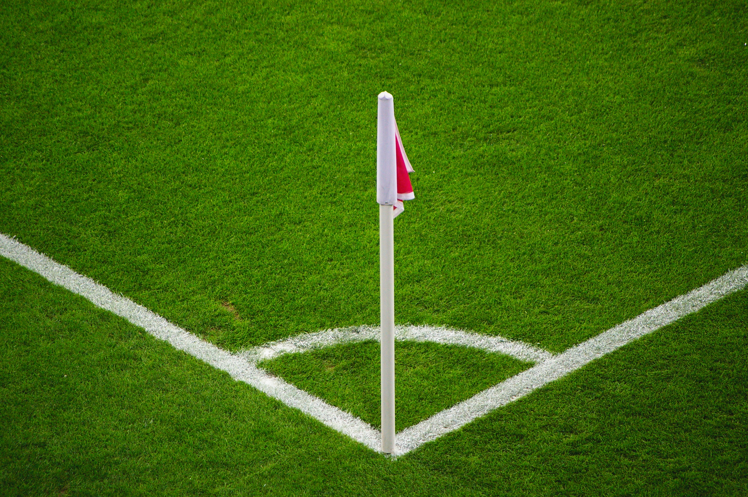 Ein Fußballfeld mit grünem Rasen, weißen Begrenzungslinien und einem weißen Pfosten mit einer roten und weißen Flagge in der Mitte des Strafraums.