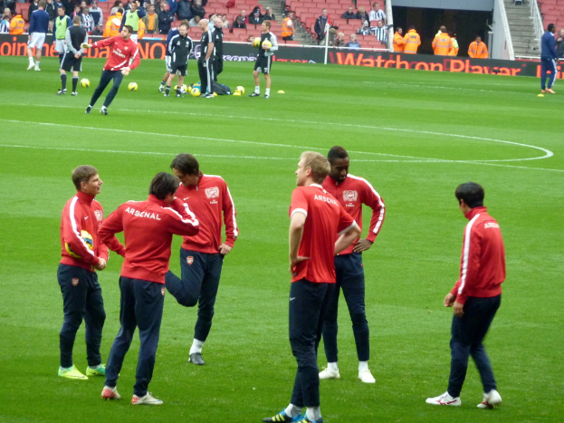 Eine Gruppe von Spielern auf einem grünen Feld mit Footballs und einer Zuschauermenge im Hintergrund.