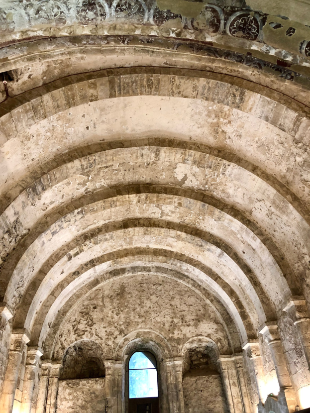 Innere eines alten Gebäudes mit gewölbter Decke, Überdächer, Säulen, Lüster und Fenster, mit detaillierten Wanddesigns und warmem natürlichem Licht.