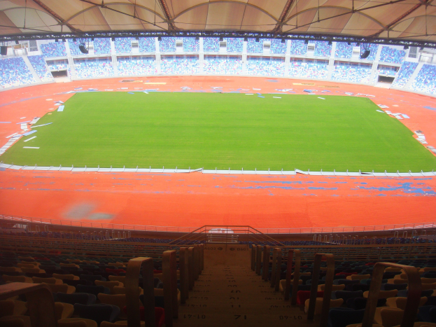 Großes Stadion voller Zuschauer mit Sitzreihen, Geländern, Treppen und Dach, mit sichtbarem Spielfeld in der Mitte.
