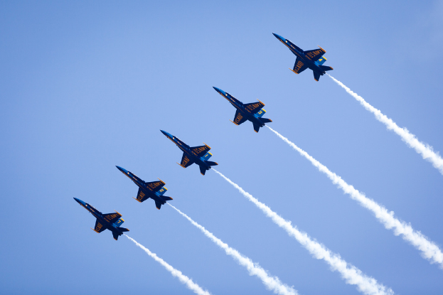 Mehrere blaue und gelbe Jets, die in einem blauen Himmel fliegen und Rauch freisetzen.
