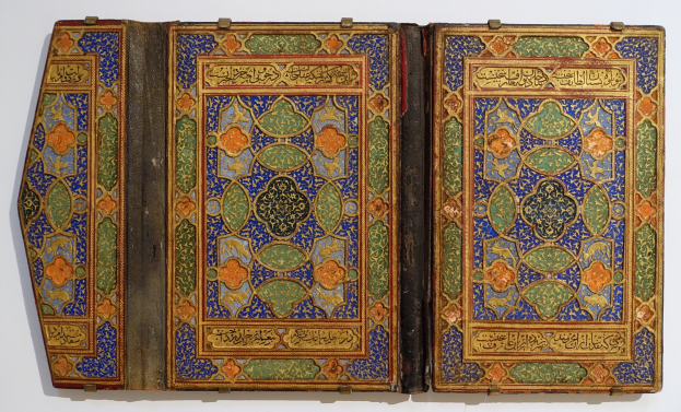 Ein offenes Buch mit detaillierter islamischer Kalligraphie und bunten Malereien, vor einem wei├čen Hintergrund.