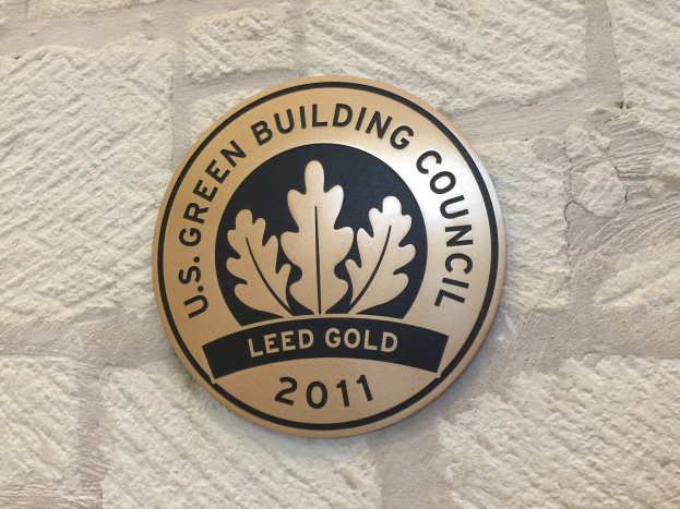Das Logo des U.S. Green Building Council an der Seite eines Gebäudes, das ein grünes Schild mit weißer Umrandung, fetten schwarzen Text und einen umgebenden Lorbeerkranz zeigt.