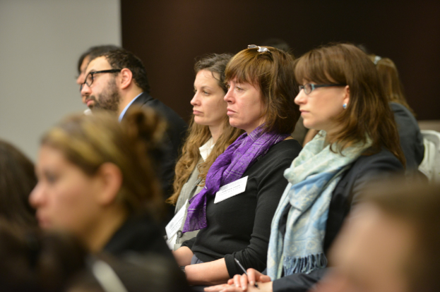 Frauen sitzen in Stühlen mit einer Person im Anzug im Hintergrund, der Vordergrund ist unscharf.